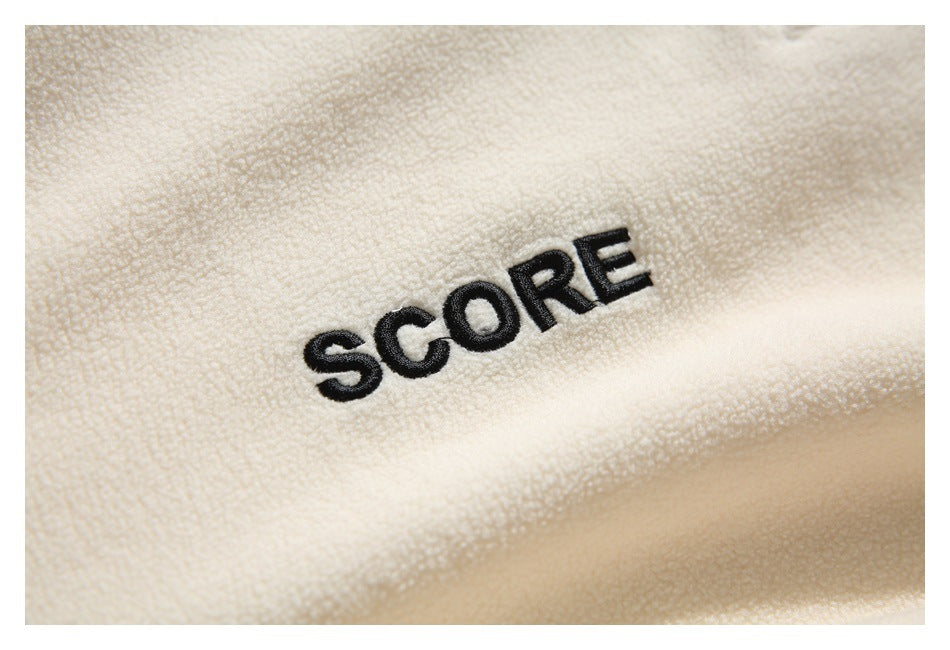 Close-up of cream textured fabric with black embroidered “SCORE” lettering.