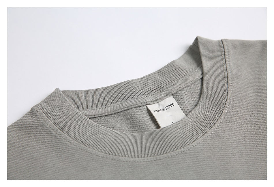 Close-up of a gray T-shirt crew neck, ribbed collar, stitching, and a white label reading “MADE IN CHINA.”