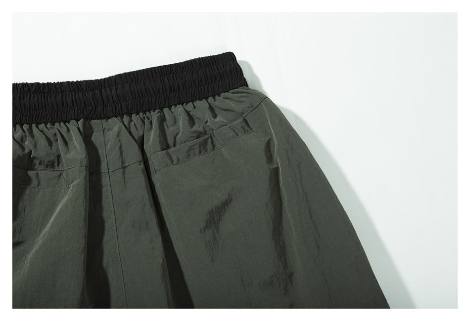 Close-up of a dark olive garment with a wide black elastic waistband and a stitched pocket.