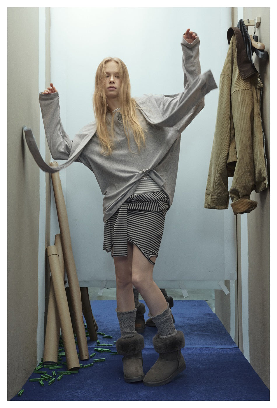 Model in an oversized gray top and black-and-gray striped skirt, arms raised to show the loose sleeves.