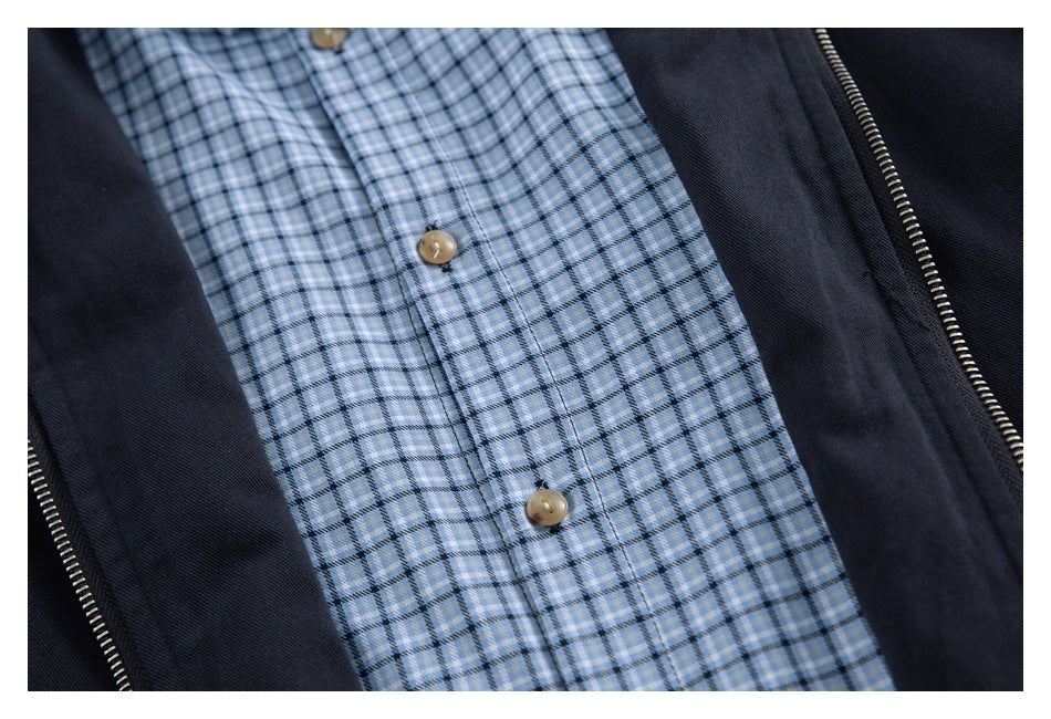Close-up of the light blue plaid button-front shirt beneath an open dark navy jacket with a zipper.