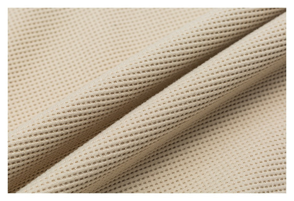 Close-up of beige fabric with a small, evenly spaced perforated knit texture, folded into soft ridges.