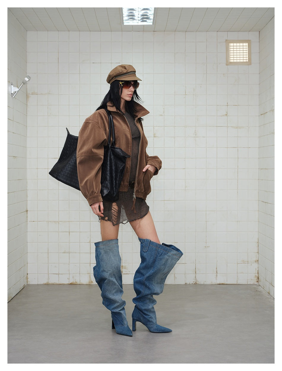 Three-quarter view of a model wearing a brown jacket with a dark distressed skirt and oversized blue denim boots.