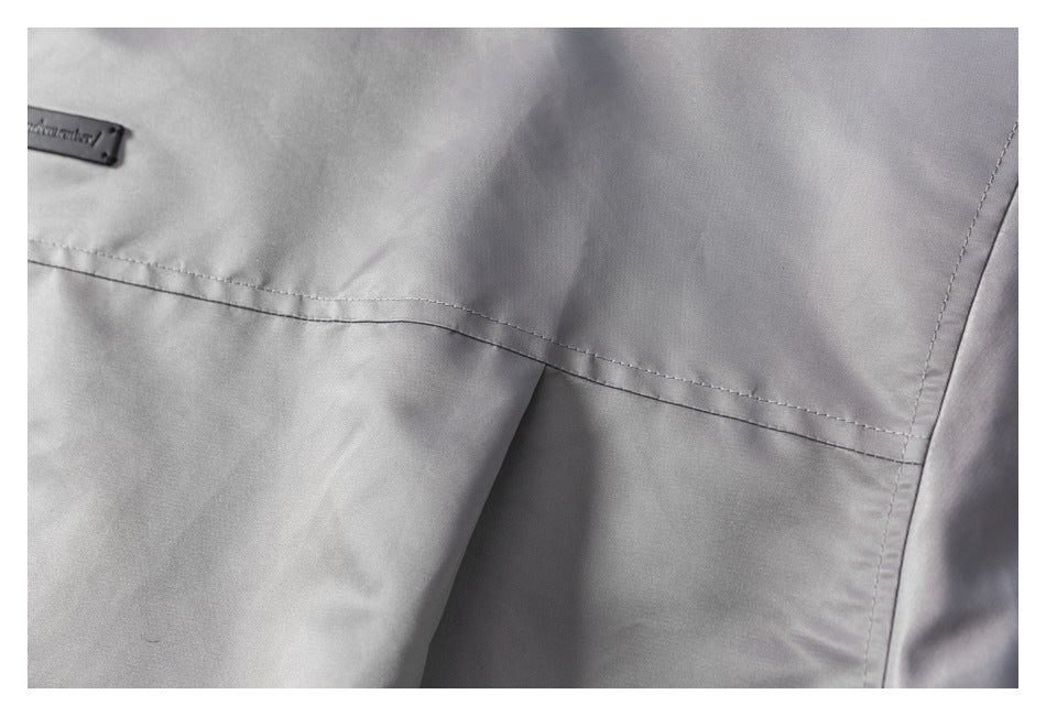 Close-up of light gray garment fabric with a diagonal stitched seam, overlapping panel, and small black label.