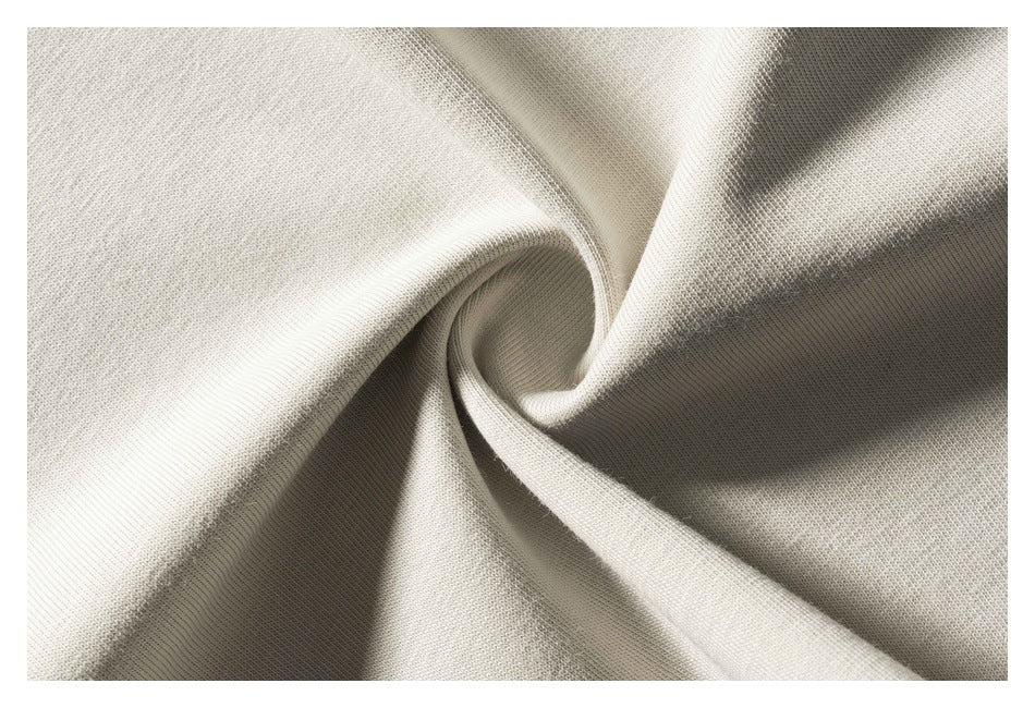 Extreme close-up of light beige T-shirt fabric gathered into folds, showing its knit texture.