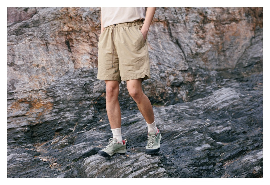 Model wearing tan elastic-waist shorts with a drawstring and side pockets, shown at a slight angle outdoors.