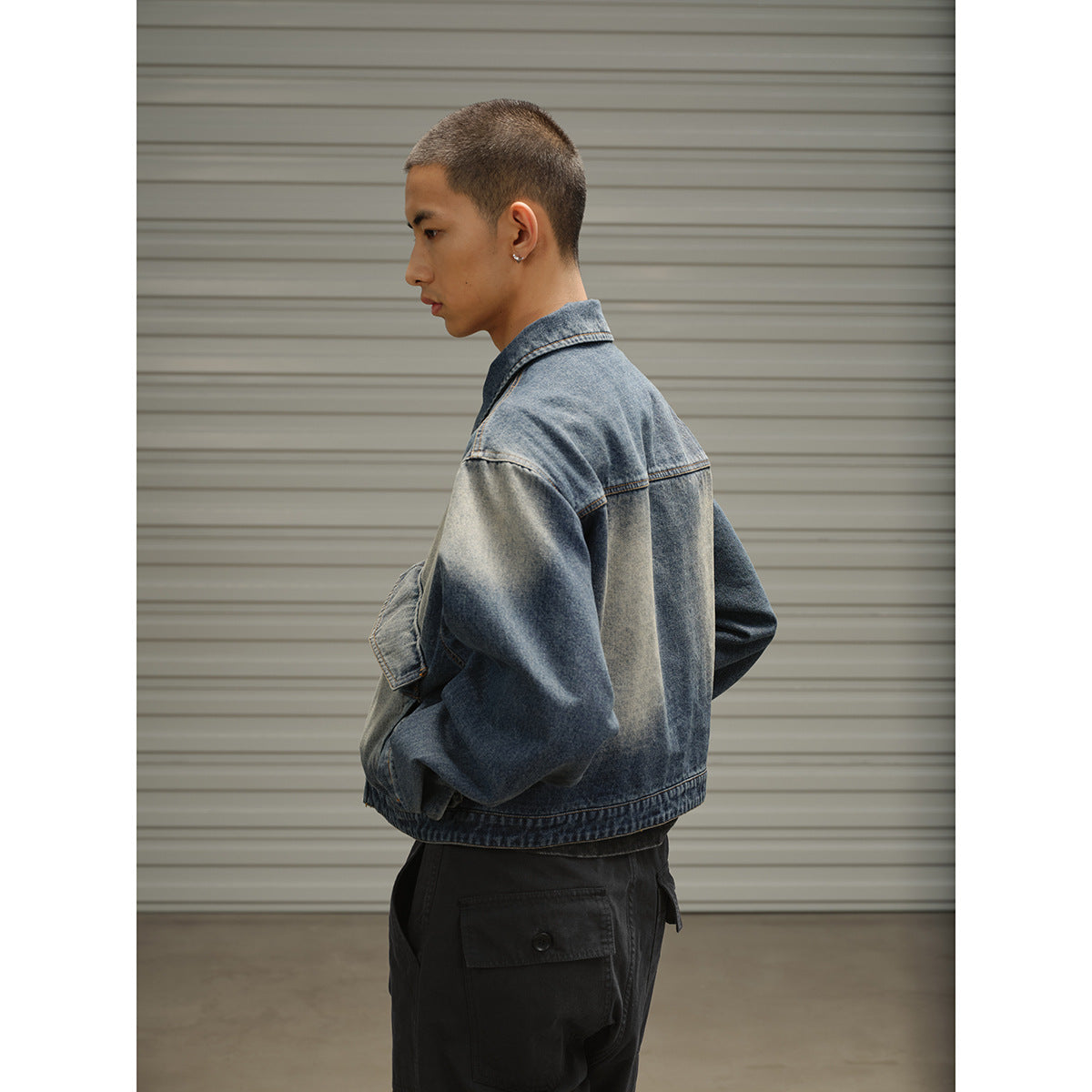 Model wearing an oversized faded blue denim jacket, shown from the side and back with black cargo trousers.
