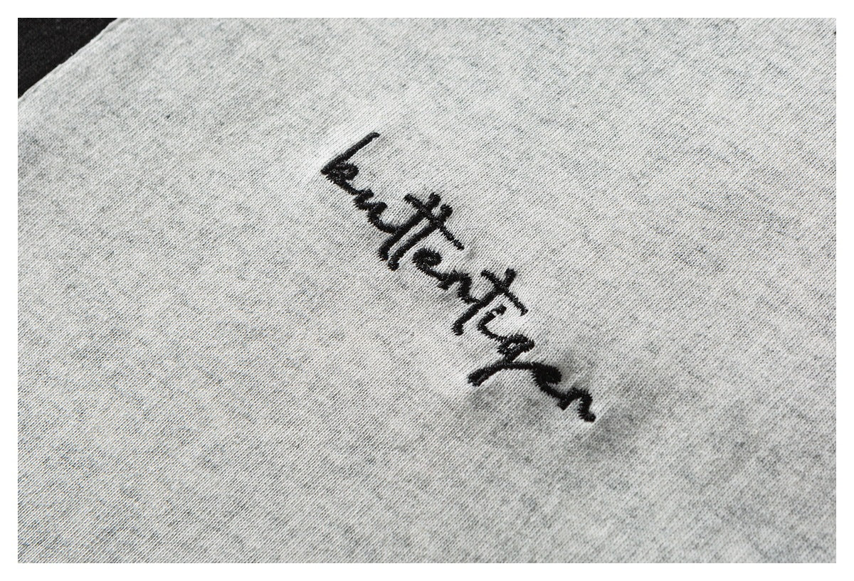 Black cursive embroidery on heather-gray garment fabric.