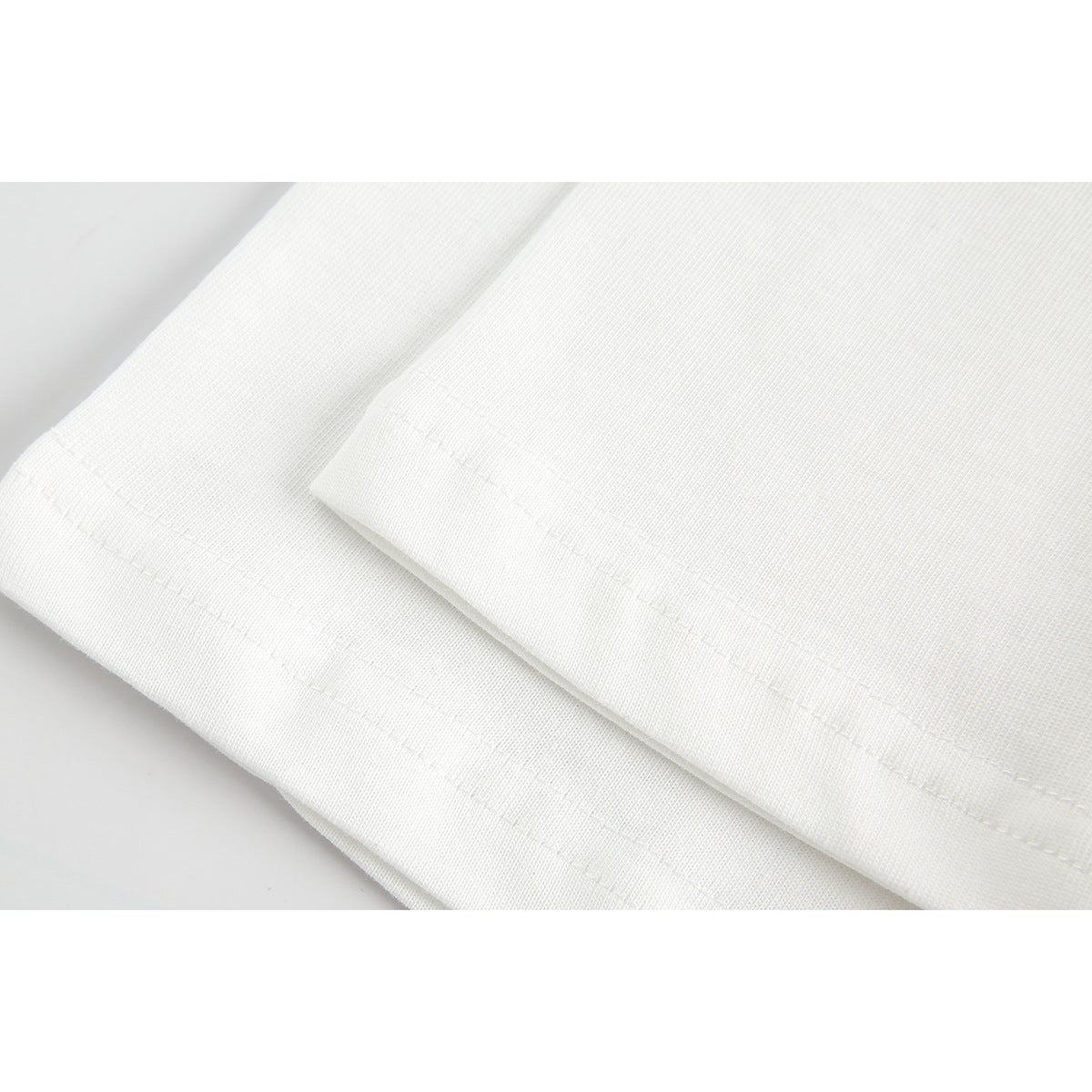 Close-up of white T-shirt fabric and folded hems showing parallel stitching.