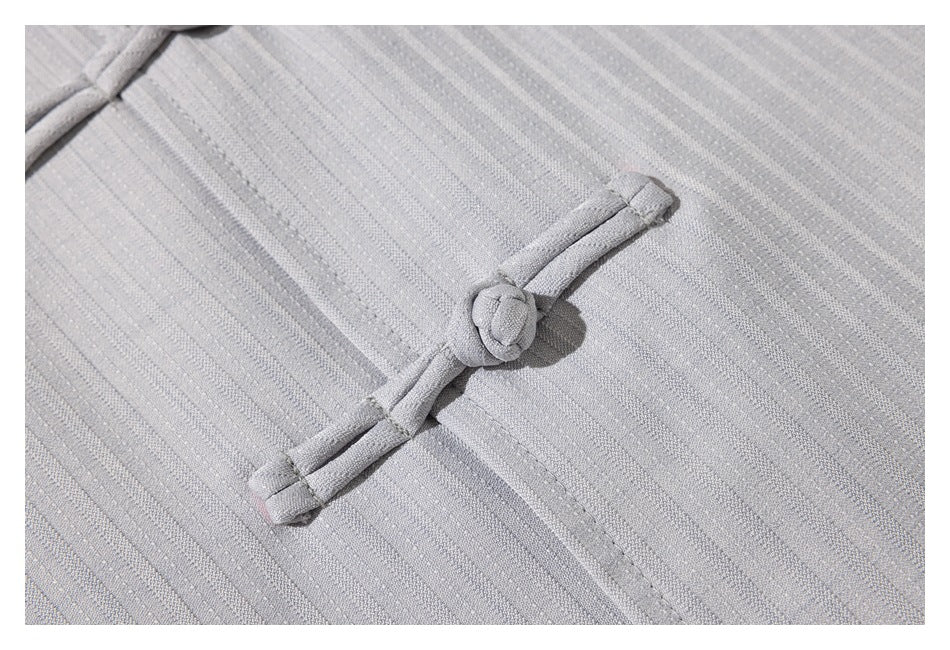 Close-up of a pale gray fabric frog closure against a subtle striped texture.