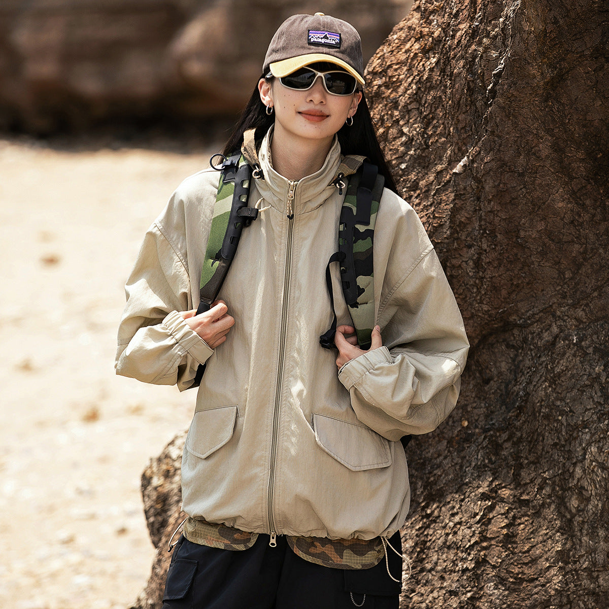 Woman wearing a loose beige hooded zip jacket with large flap pockets and elastic cuffs.