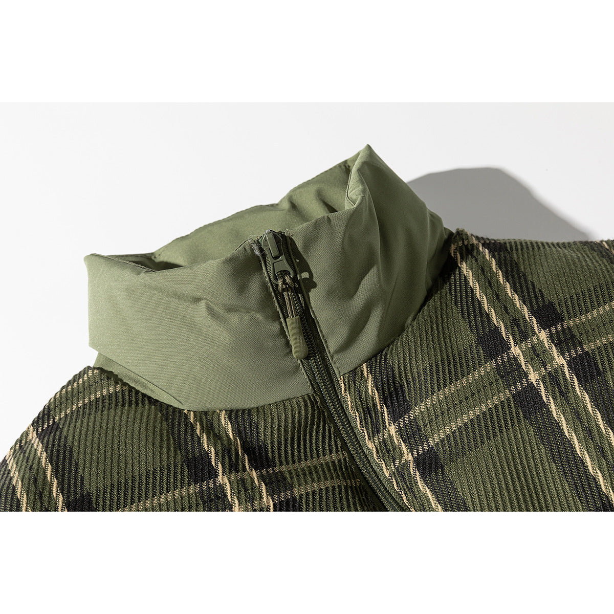 Close-up of an olive-green stand collar and zipper beside dark green and tan plaid jacket panels.