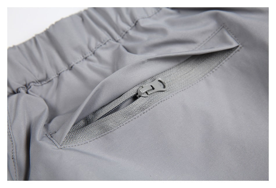 Close-up of light gray trousers with an elastic waistband and a slanted pocket with a gray zipper.