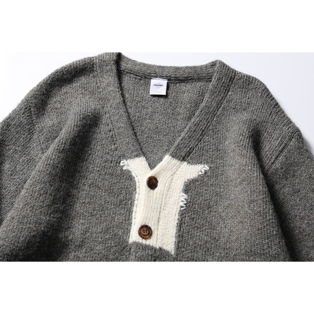 Close-up of a gray knit cardigan front with a cream button placket and two brown buttons.