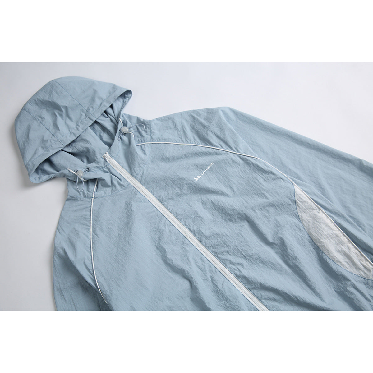 Close-up of a pale blue hooded jacket with an angled white zipper, drawcords, contrast piping and a small chest logo.
