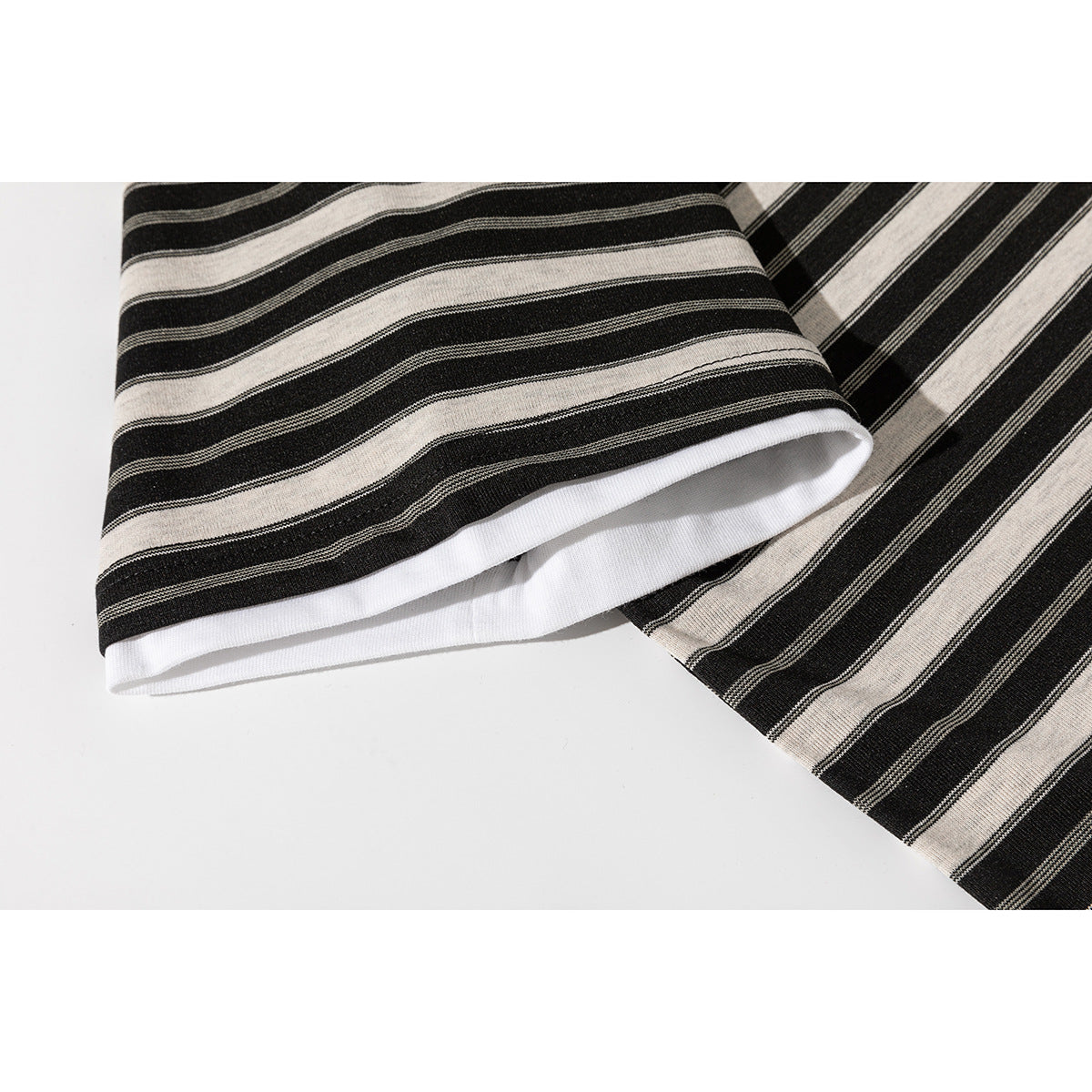 Close-up of the black and beige striped T-shirt sleeve cuff, showing its white inner facing.