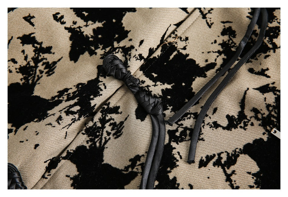 Close-up of a black braided knot fastener and straps against tan fabric with a black abstract floral pattern.