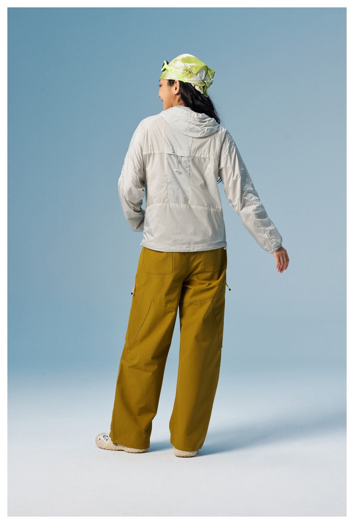 Rear view of a model wearing a light gray hooded jacket and mustard yellow cargo pants.