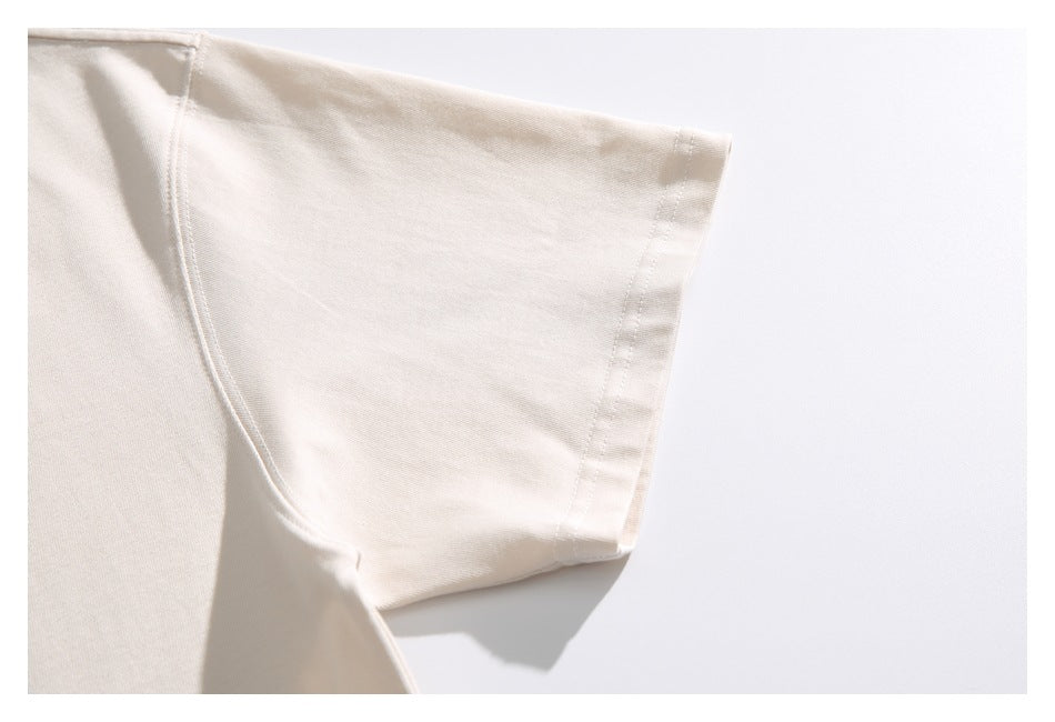 Close-up of an ivory T-shirt sleeve and stitched cuff against a pale background.