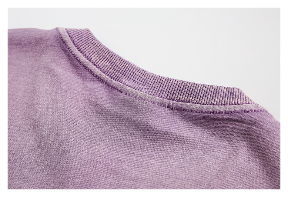 Close-up of the ribbed crew neckline and shoulder seam of a lavender garment.