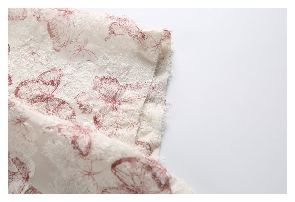 Close-up of an ivory garment edge with raised white texture and dusty rose butterfly print.