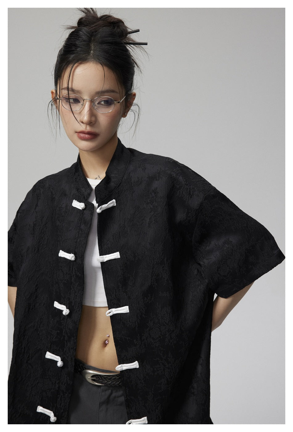 Close view of a model wearing a black textured jacket with white frog closures and short sleeves.