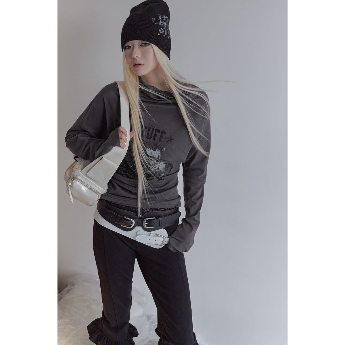 Model wearing a charcoal draped long-sleeve graphic top, black ruffle-hem pants, and a black beanie.
