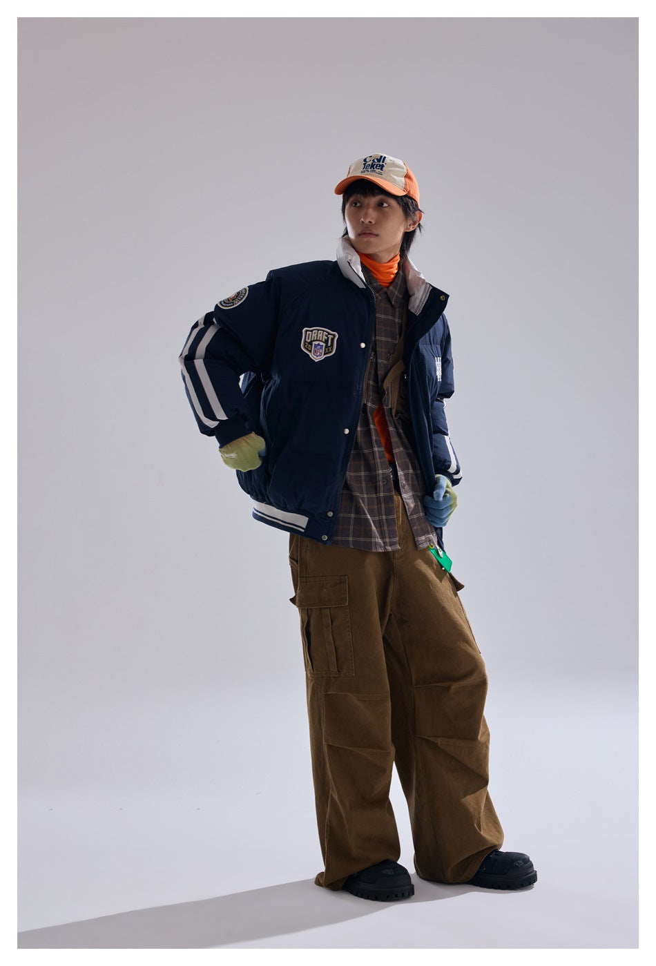 Model wearing a navy padded jacket with white sleeve stripes and patches, shown in a front three-quarter view.