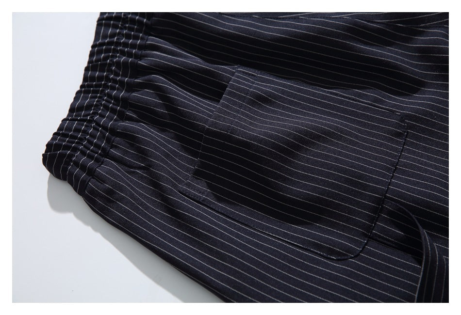 Close-up of a large rectangular pocket on dark pinstriped trousers beside the gathered waistband.