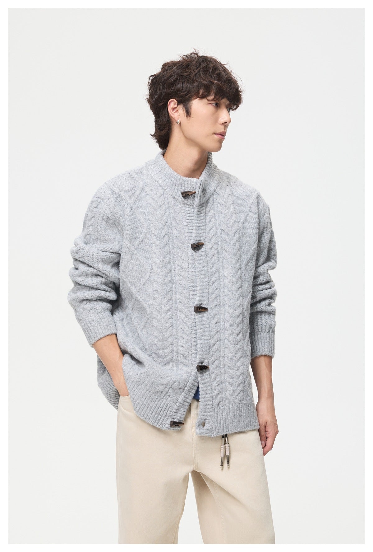 Model wearing a light gray cable-knit cardigan with a stand collar, toggle closures, and cream trousers.