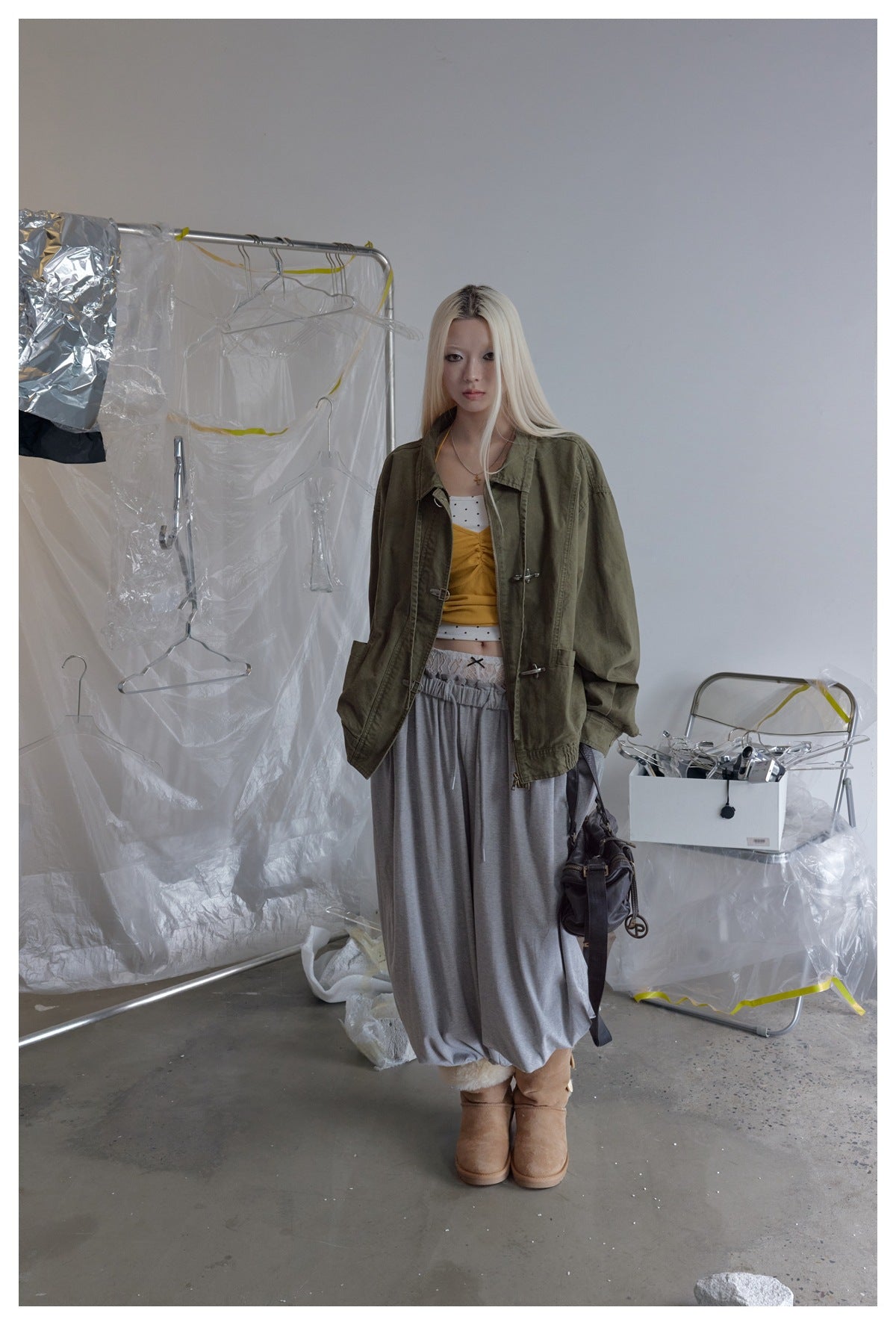 Model wearing the olive green hook-closure jacket open over a yellow top, gray skirt and tan boots