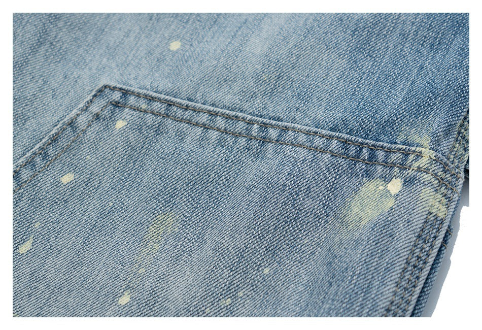 Close-up of a stitched back pocket on light blue denim jeans with scattered pale distress marks.
