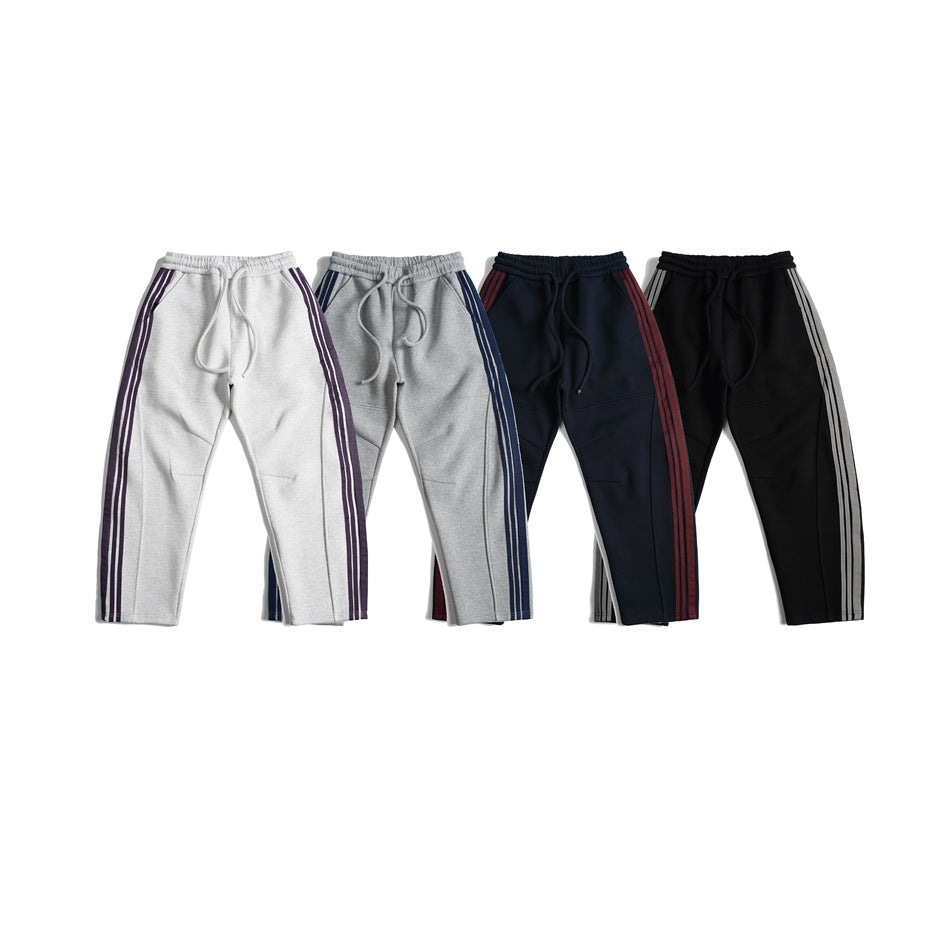 Four pairs of jogger pants shown from the front in light gray, gray, navy, and black, each with contrasting side stripes.
