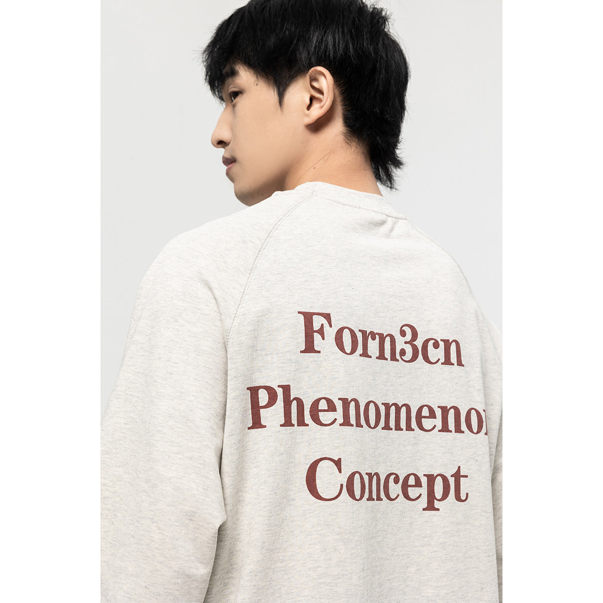 Close view of the back of an off-white T-shirt with large burgundy “Form3cn Phenomenon Concept” lettering.