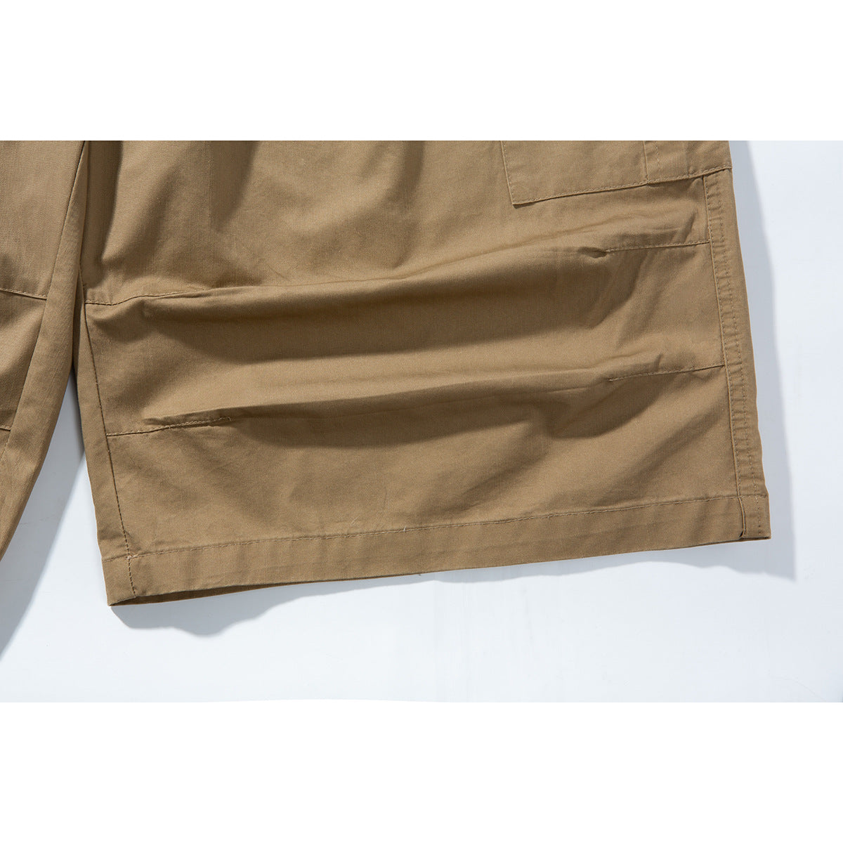 Close-up of the tan shorts’ lower leg, showing a large stitched cargo pocket and hem.