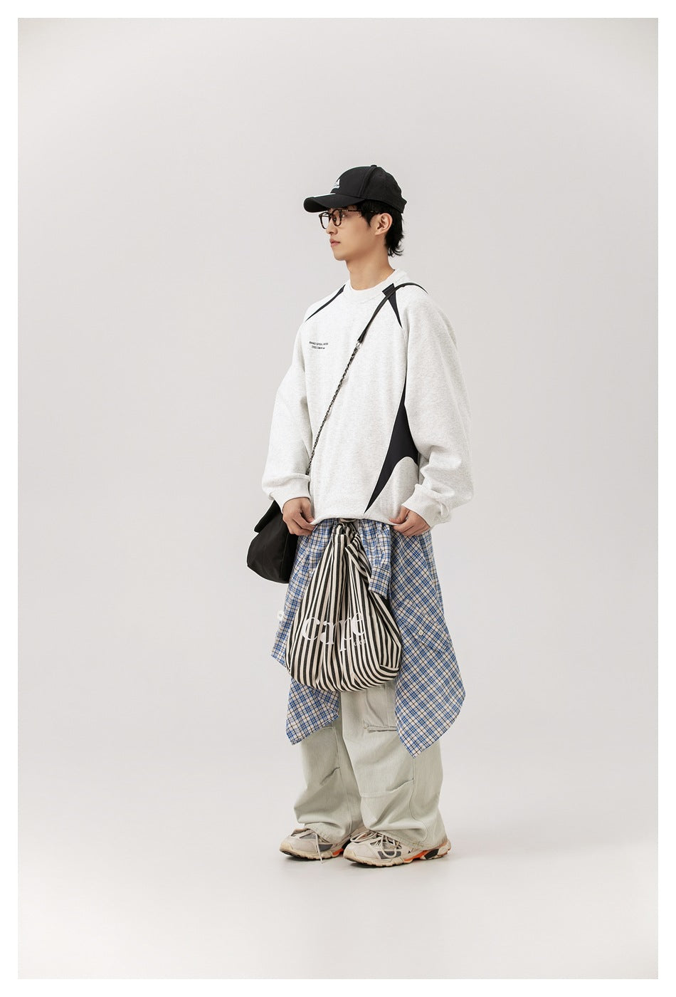 Side view of a model wearing a light gray sweatshirt with black curved panels and a blue plaid shirt tied at the waist.