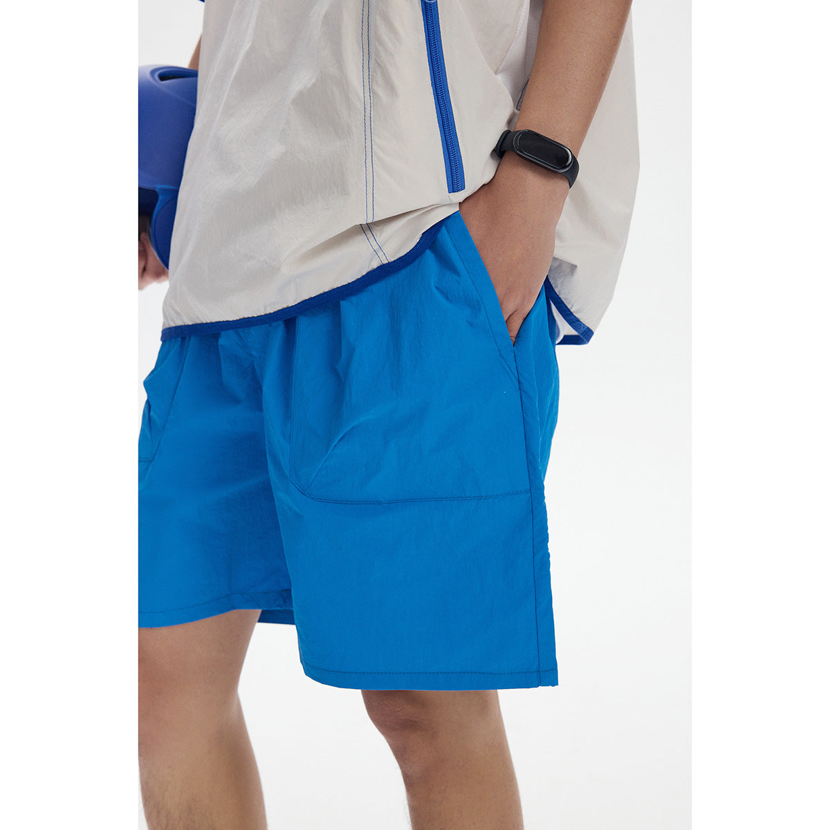 Close-up of bright blue shorts with a large pocket beside an ivory shirt with blue zipper trim.