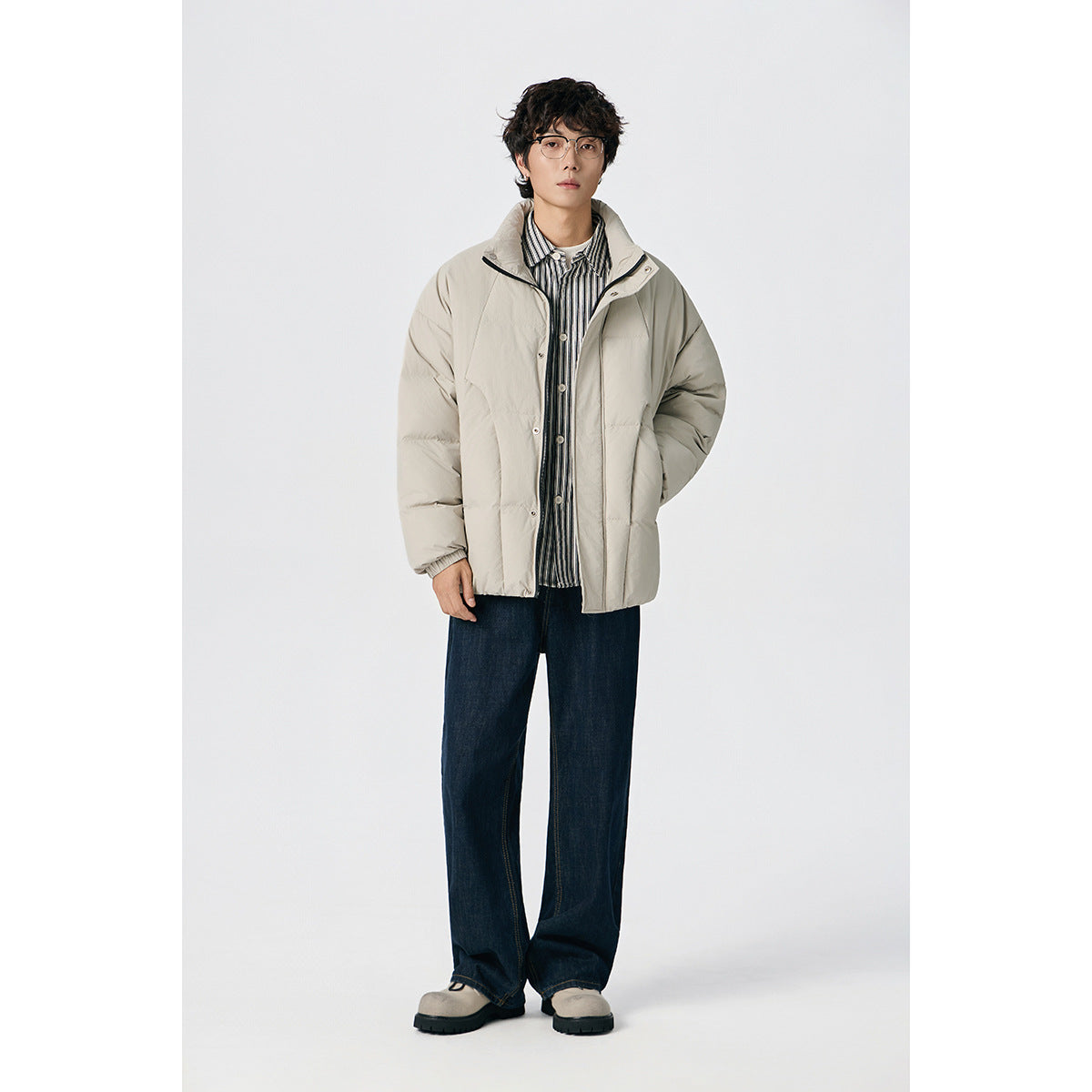 Model wearing a light beige padded jacket over a striped shirt with dark wide-leg jeans, front view.