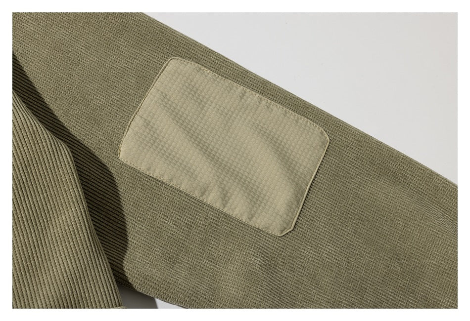 Close-up of a rectangular elbow patch on the sleeve of an olive pullover.