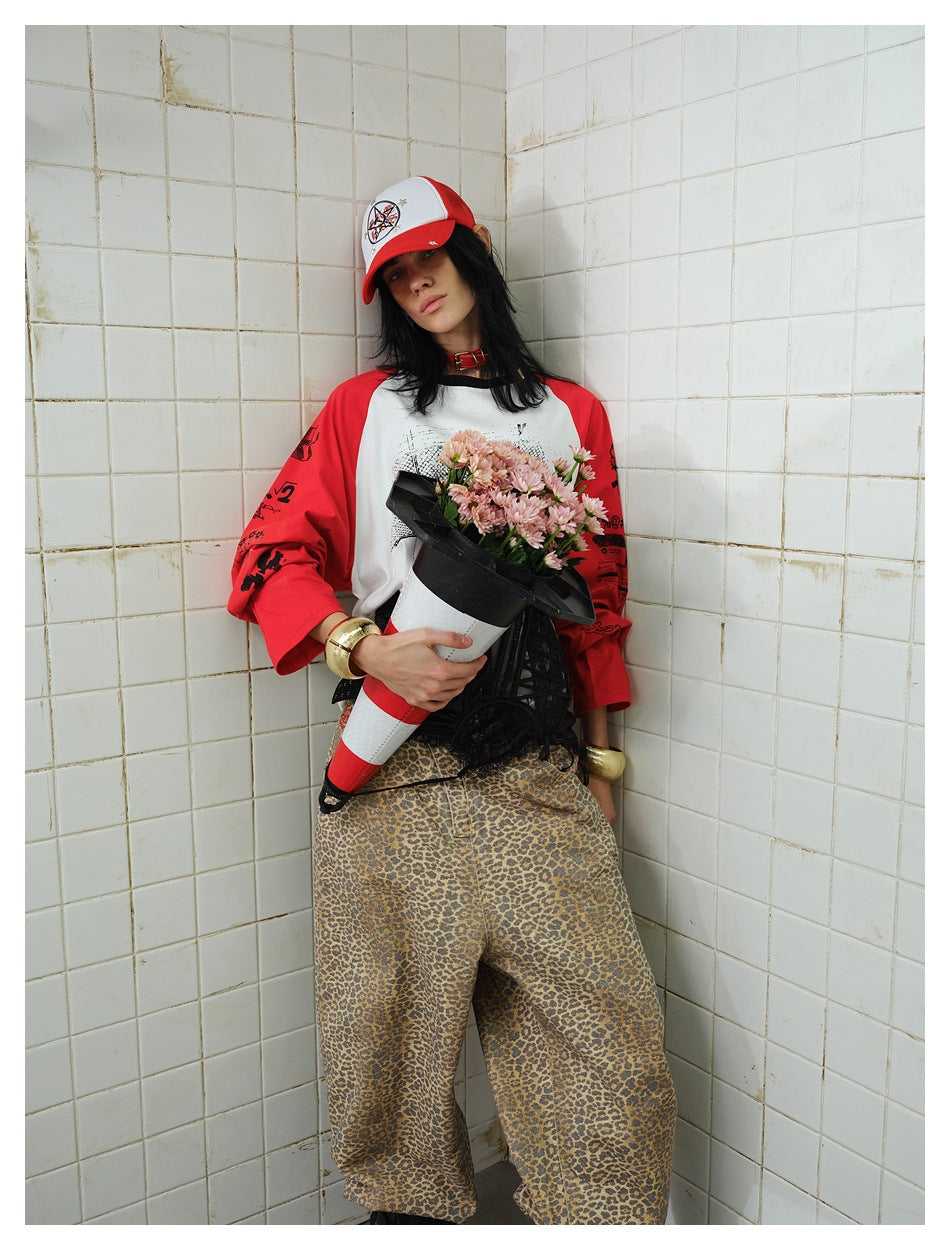 Model in a red and white raglan long-sleeve top with a cap and leopard pants, holding flowers in a traffic cone