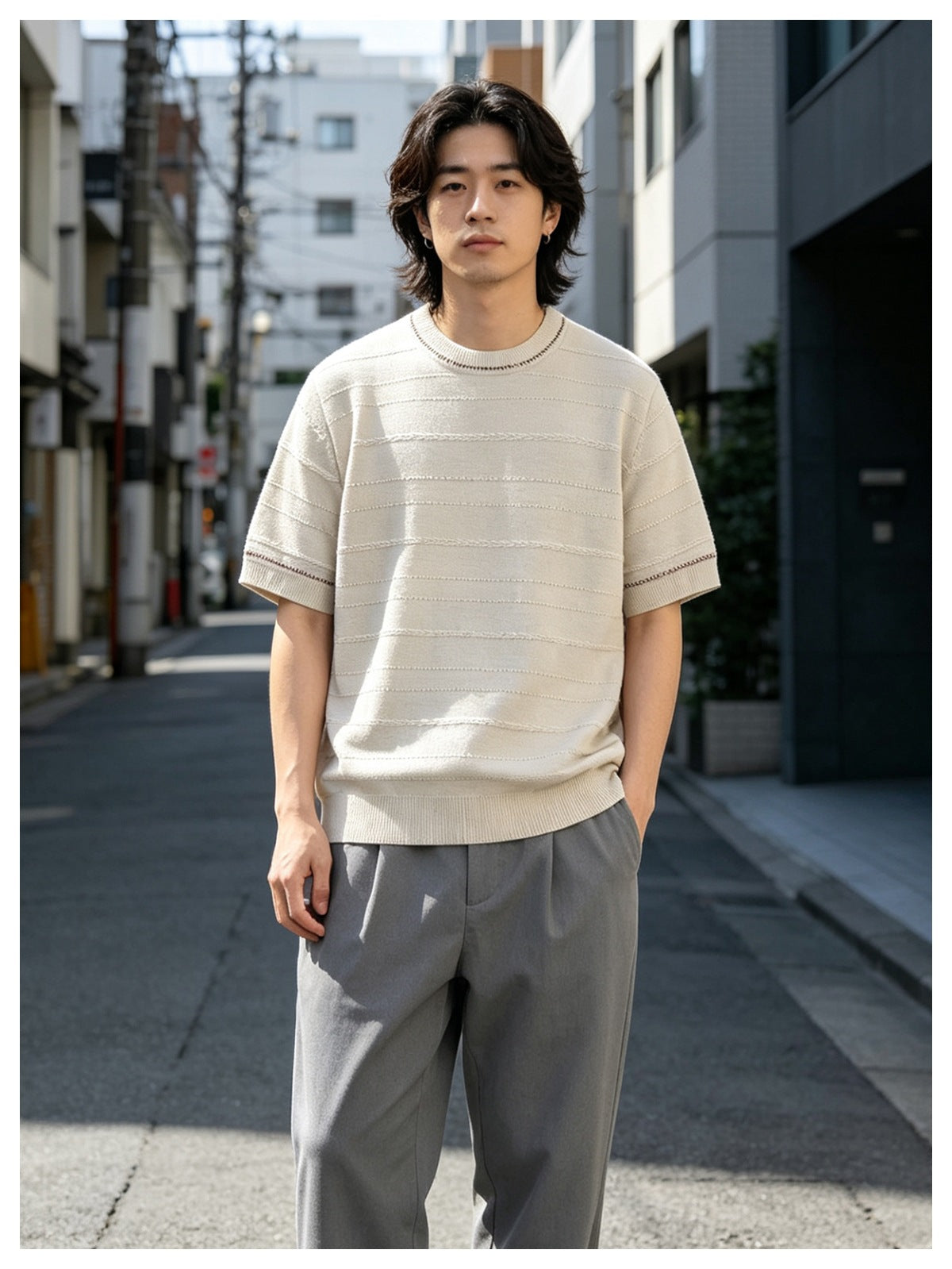 Man wearing beige short-sleeve textured knit top with contrast neckline stitching and gray trousers on a city street
