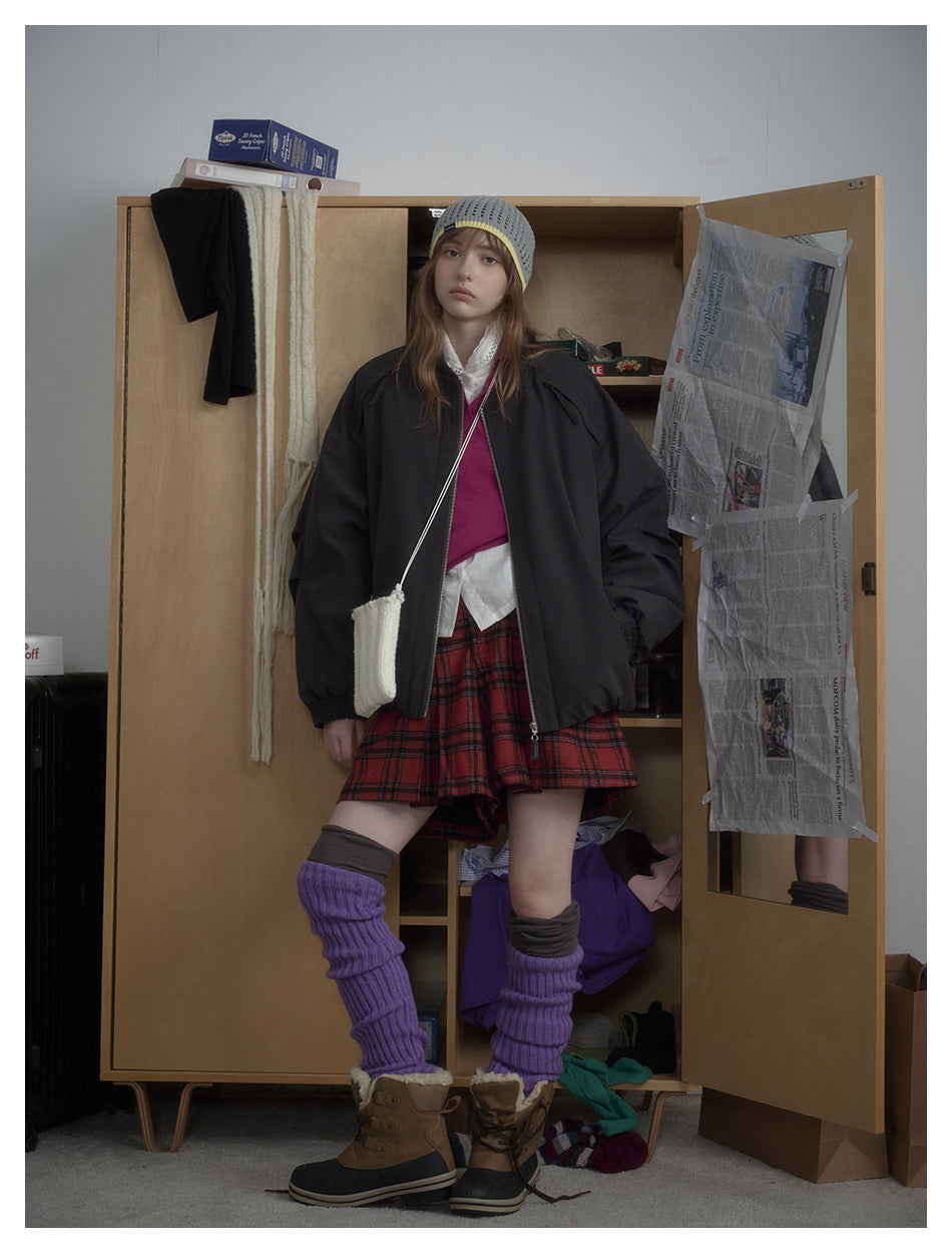 Model wearing the black zip bomber jacket open over a pink vest, red plaid skirt and purple leg warmers, front view