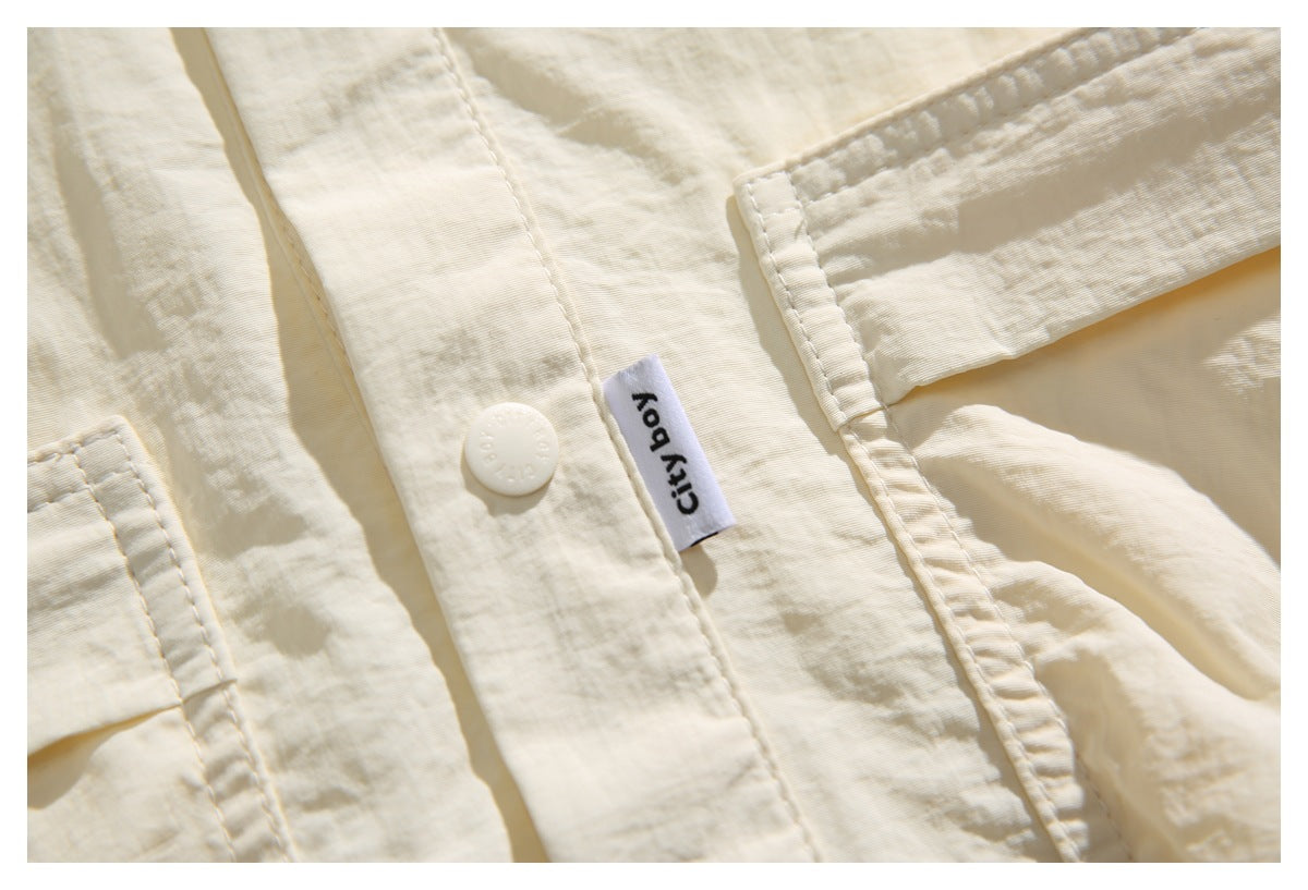 Close-up of an ivory shirt placket with a button, stitched city boy label, and pocket edge.