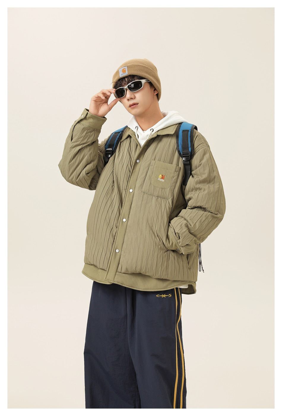 A model wears an olive quilted button-front jacket with a chest pocket over a white hoodie.