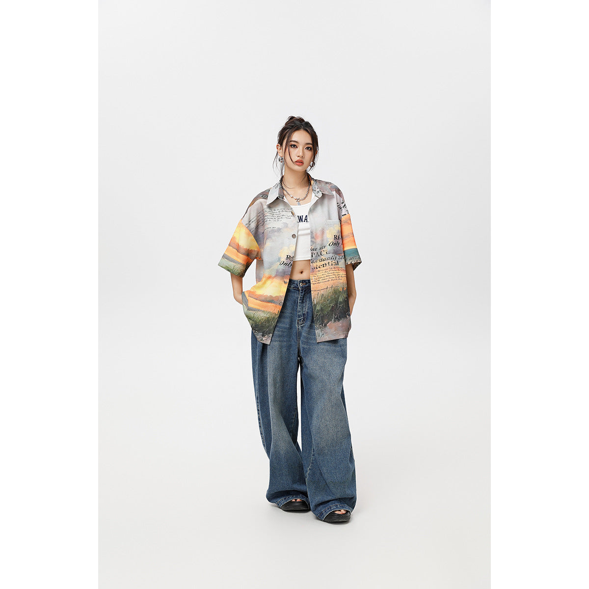 Full-length front view of a model wearing a multicolored printed short-sleeve button-up shirt and wide-leg blue jeans.