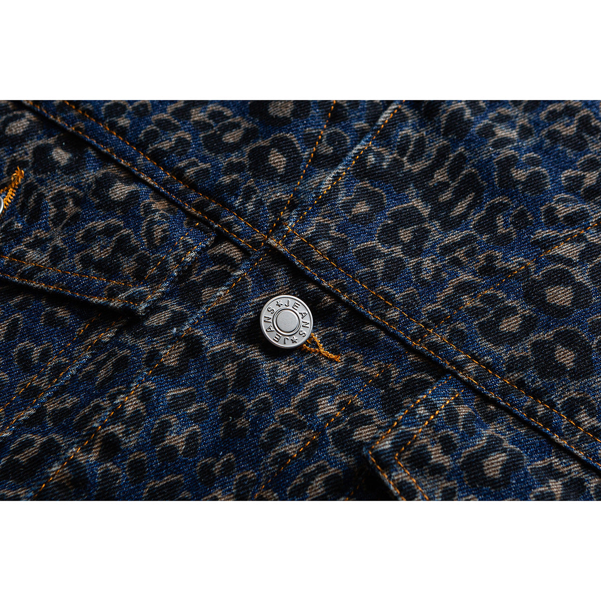 Close-up of a silver button and orange-stitched seams on dark blue leopard-print denim.