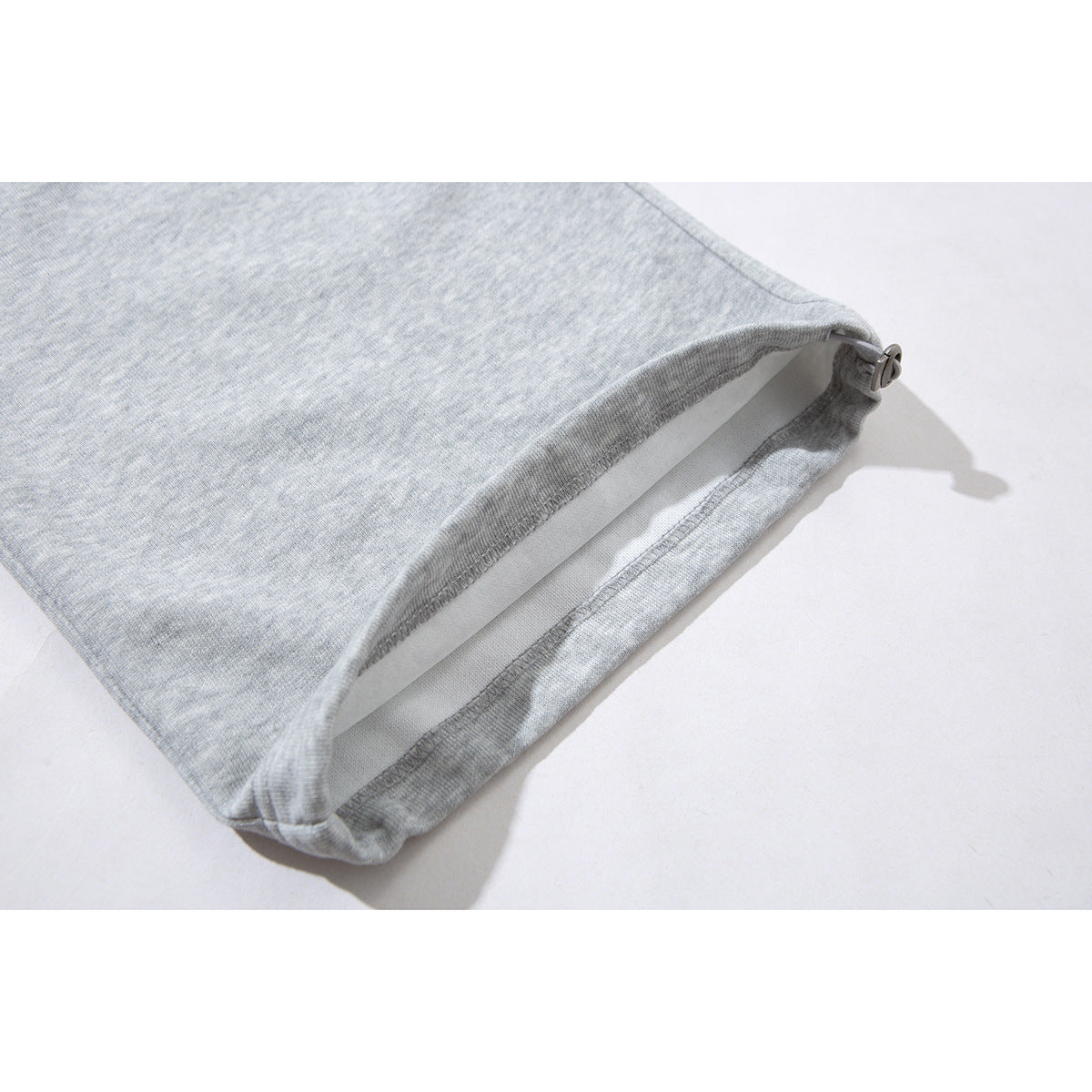 Close-up of the light gray sweatpants leg opening, showing the hem and small side adjuster.