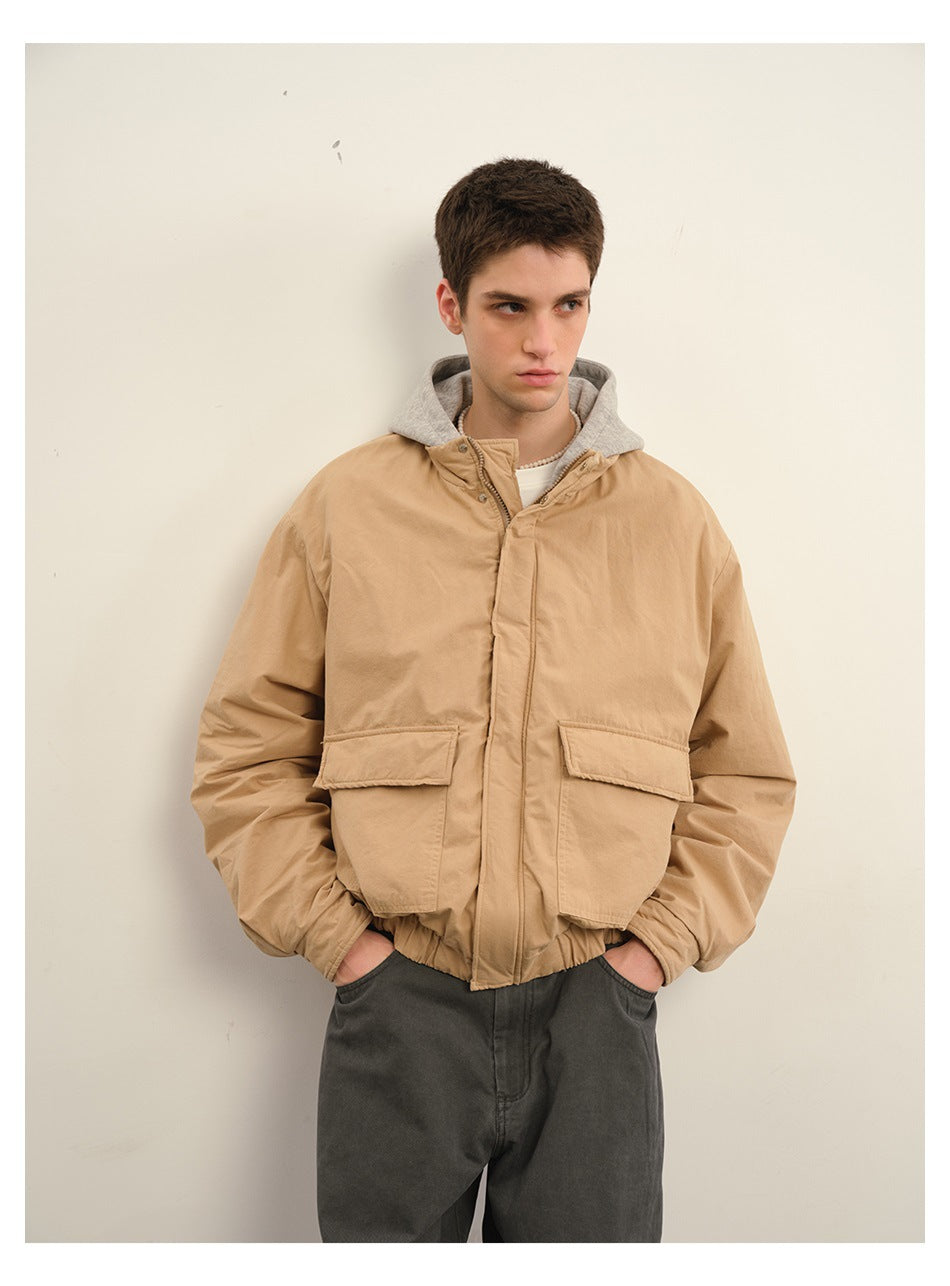 Model wearing a tan hooded jacket with a gray hood, front view with large flap pockets.