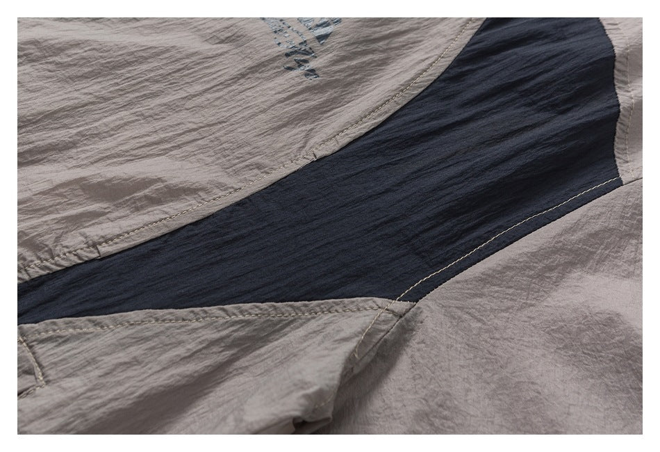 Close-up of taupe-gray garment panels joined by a dark navy contrast insert and visible stitching.