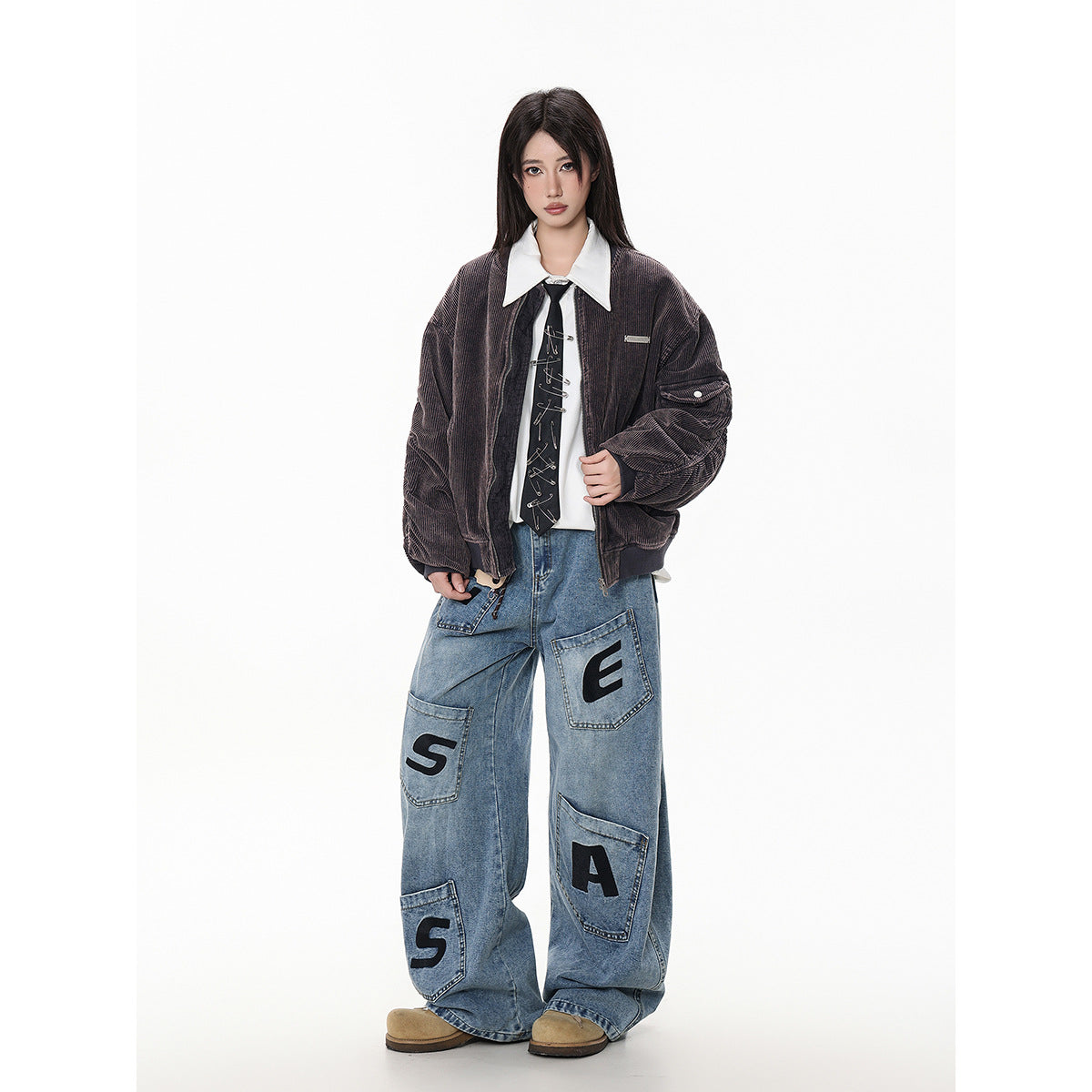Model wearing an open dark brown bomber jacket over a white shirt and tie, with oversized letter-patch jeans.